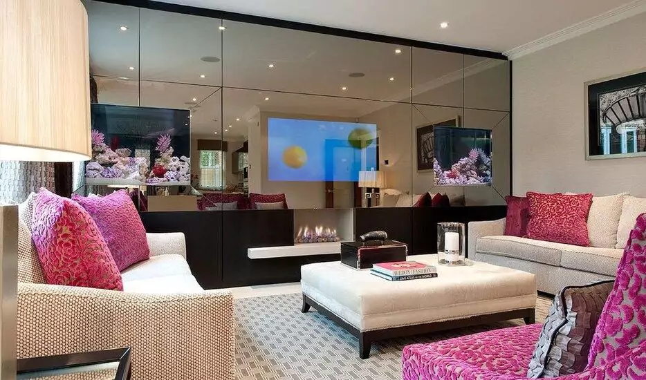 Pink pillows on a couch with a large leather Ottoman at the center and a wide mirror TV.
